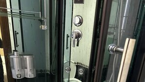 Et brusebad i hjørnet med glasvæg, et hvidt badekar og et toilet, der kan ses igennem glasset.