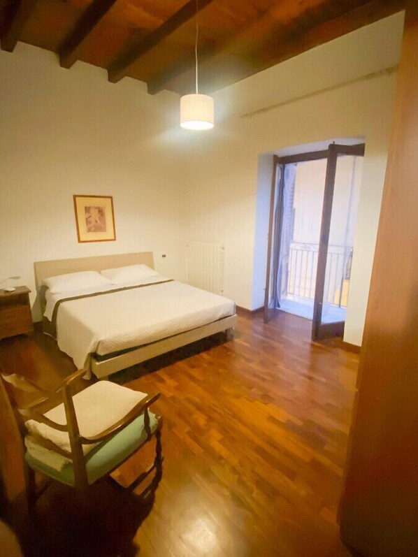 A bedroom with a wooden floor, a bed, a chair, a radiator, and a window with a view.
