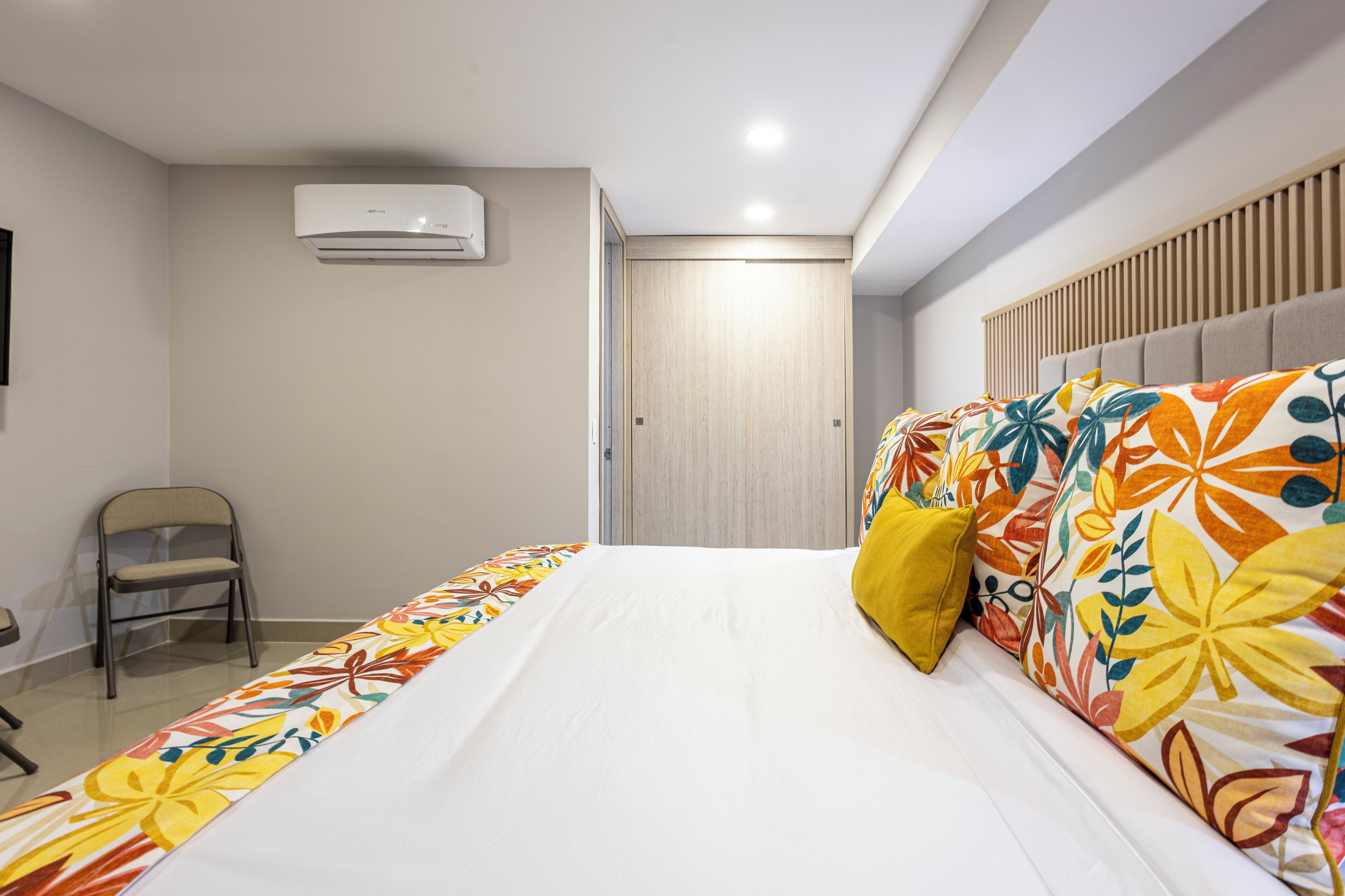 Quarto de hotel com cama, cadeira, guarda-roupa e ar condicionado.