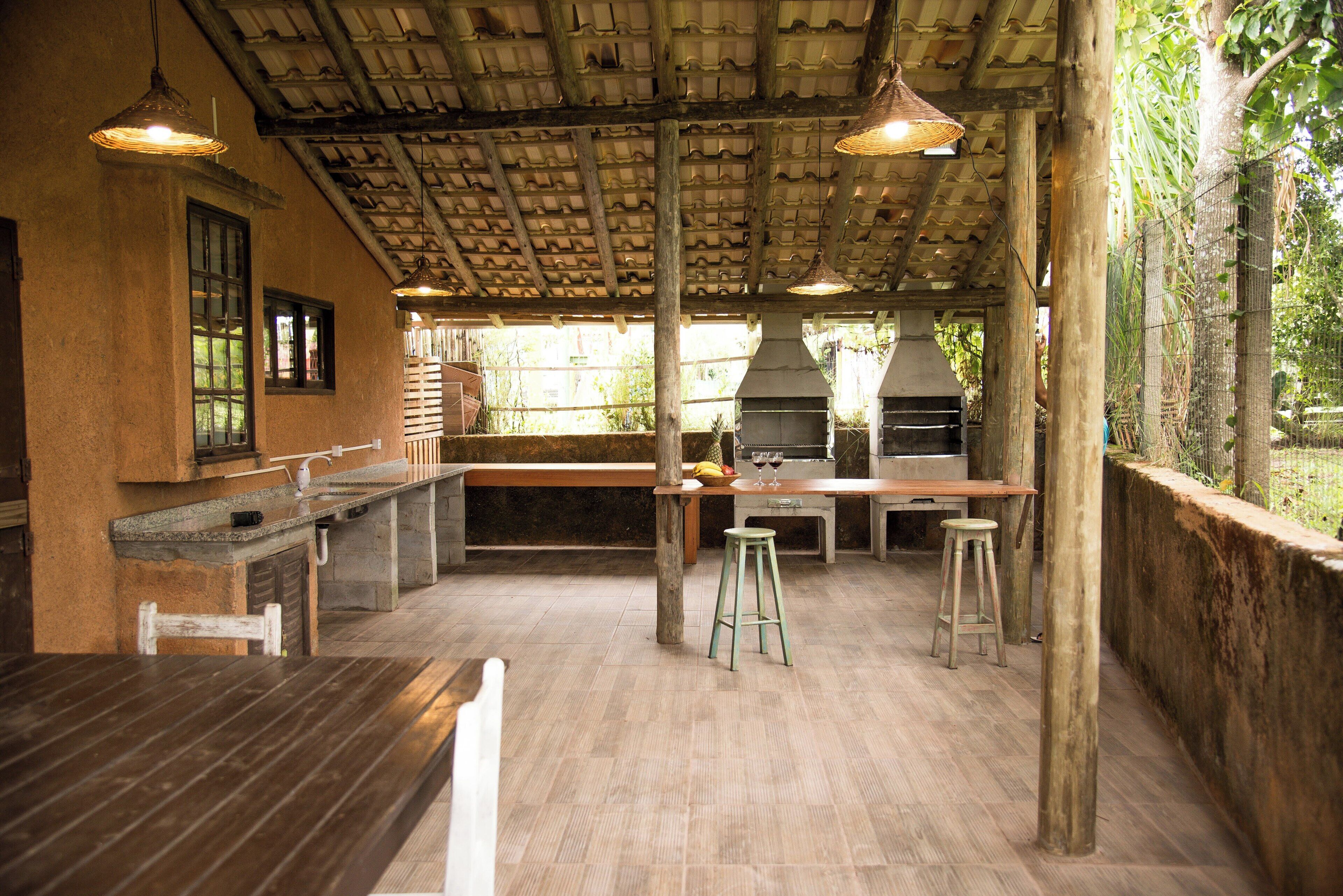 Uma área de cozinha externa com mesa de madeira, banquetas de bar e churrasqueira.