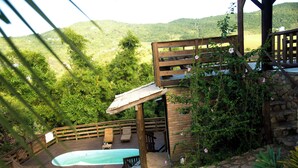 A wooden deck with a hot tub, lounge chairs, and a stone pathway leading to a pool. - Pousada La Creacion (Imbituba)