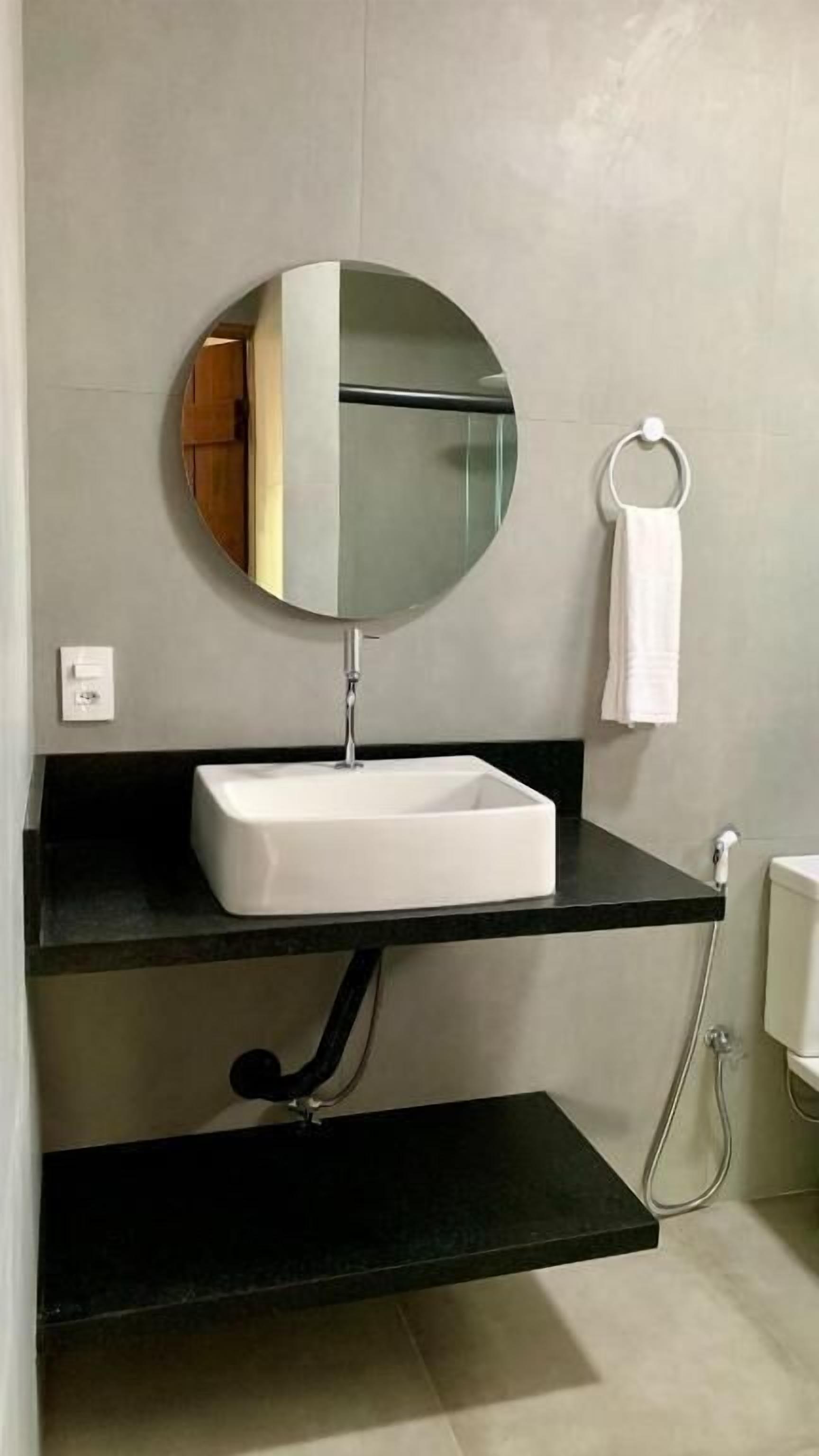 Une salle de bain moderne avec un miroir rond, un lavabo blanc et des étagères noires.