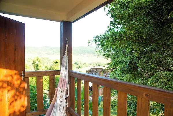 Un balcón de madera con una hamaca, con vistas a un paisaje verde exuberante y colinas distantes.