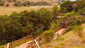 A wooden boardwalk leading through a natural landscape with trees and a distant building. - Pousada La Creacion (Imbituba)