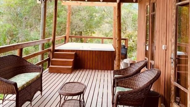 A wooden deck with wicker furniture, a hot tub, and a view of the surrounding greenery. - Pousada La Creacion (Imbituba)