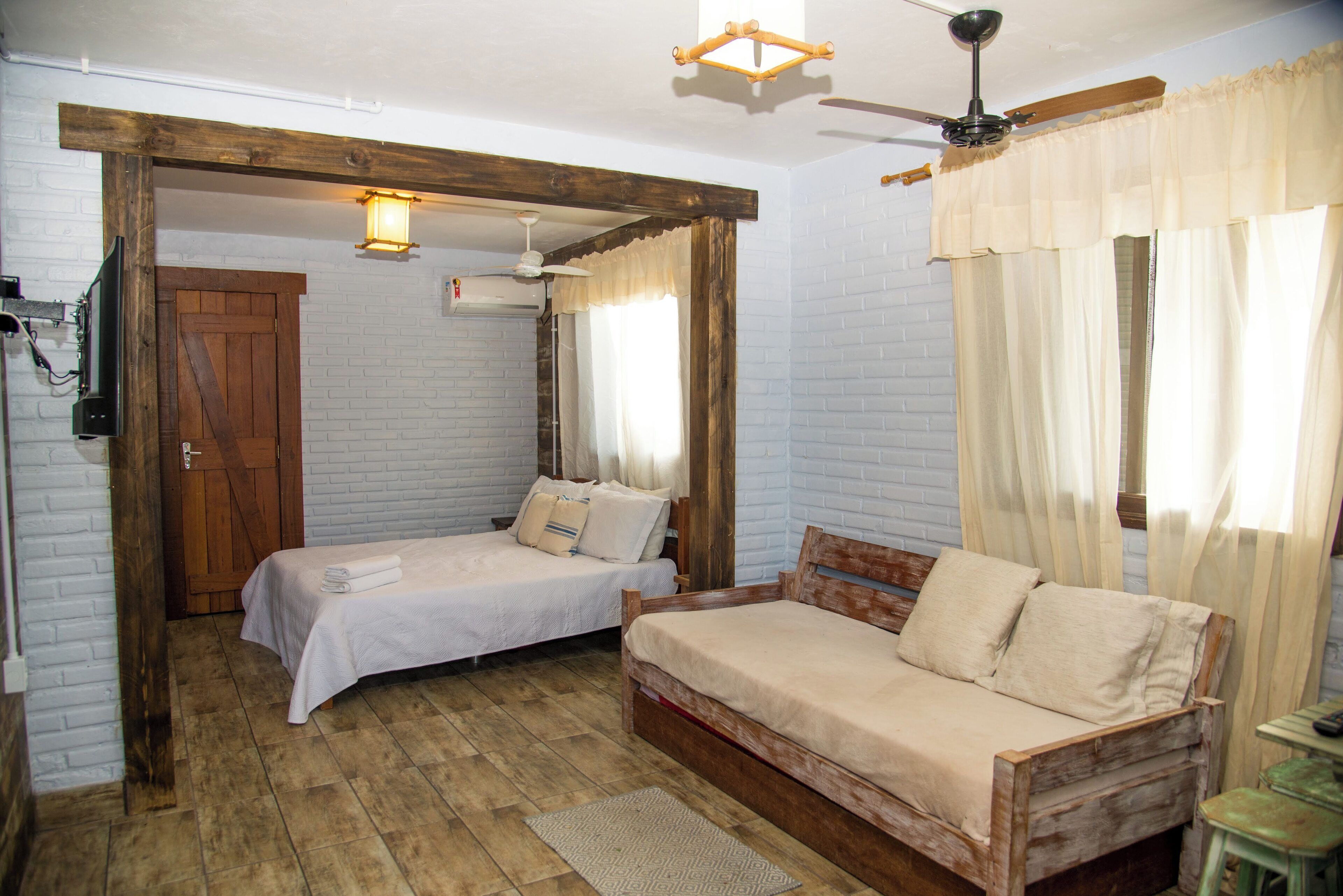 Quarto com duas camas, um ventilador de teto de madeira, uma luminária no teto e uma janela com cortinas.
