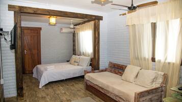 Quarto com duas camas, um ventilador de teto de madeira, uma luminária no teto e uma janela com cortinas.