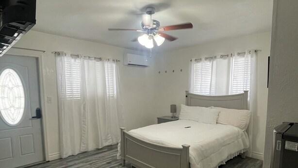 A bedroom with a bed, a ceiling fan, a window with curtains, and a door. - Luxury Studio with Private Entrance Near Hard Rock Stadium. (Miami Gardens)