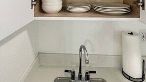 A kitchen with a sink, a paper towel dispenser, and shelves with plates, bowls, and glasses. - Luxury Studio with Private Entrance Near Hard Rock Stadium. (Miami Gardens)