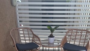 Two wicker chairs with cushions and a small table with a potted plant between them, set on a concrete patio with a white fence in the background. - Luxury Studio with Private Entrance Near Hard Rock Stadium. (Miami Gardens)