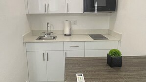 A compact kitchen with white cabinets, a microwave, a sink, and a small potted plant. - Luxury Studio with Private Entrance Near Hard Rock Stadium. (Miami Gardens)