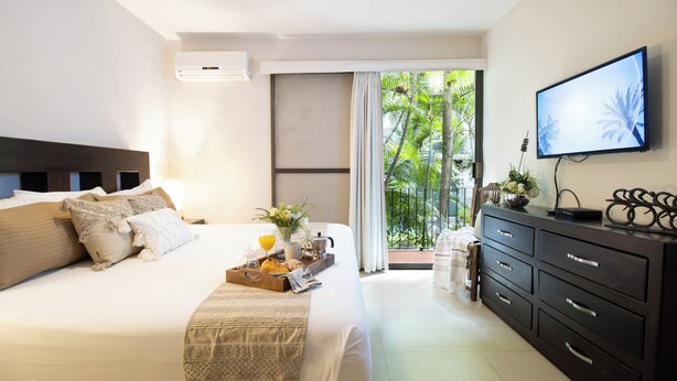 A hotel room with a bed, a dresser, a television, and a balcony with a view of palm trees. - Cozy stay Tropical Vibes near Beach (Puerto Vallarta)