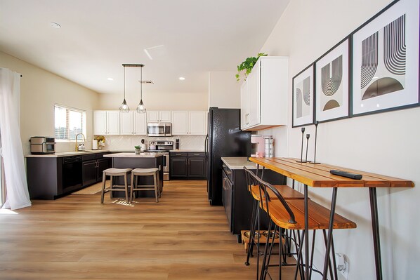A modern kitchen with a central island, bar stools, and pendant lighting. - Spacious San Tan Escape on Golf Course⛳️ PICKLEBALL & POOLS, MASSAGE CHAIR, etc!  (San Tan Valley)