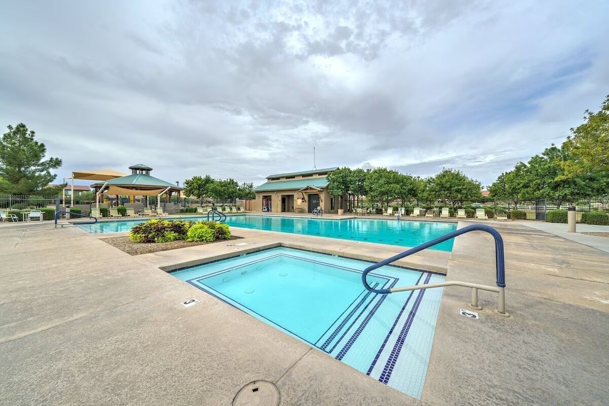 Una piscina con bordo blu, un'area relax coperta e un edificio sullo sfondo con tetto verde.
