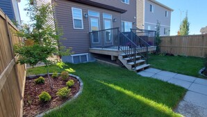 A residential backyard with a wooden deck, a small staircase, and a well-maintained lawn. - Delightful and Serene Private Studio Close to the Airport (Calgary)
