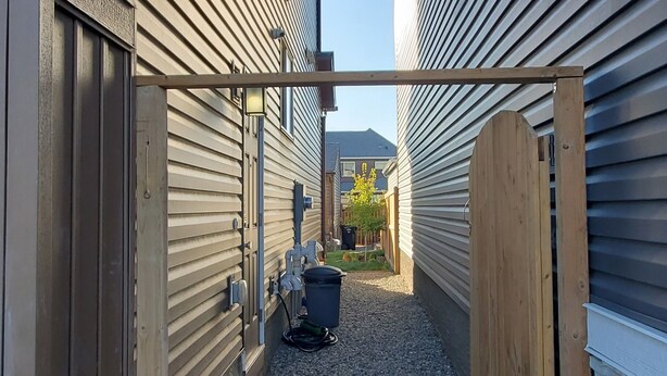 A narrow pathway between two buildings with a gravel path and a wooden fence. - Delightful and Serene Private Studio Close to the Airport (Calgary)
