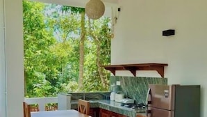 A modern kitchen with wooden furniture, a refrigerator, and a view of greenery outside. - Cocosurf House (Hikkaduwa)