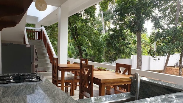 A kitchen with a marble countertop, wooden dining table, and chairs, with a view of a staircase and greenery outside. - Cocosurf House (Hikkaduwa)