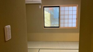 Una stanza con pavimento in tatami, una finestra con paravento scorrevole in stile shoji e un condizionatore d'aria.