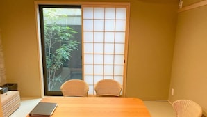 Una stanza con una porta scorrevole in stile shoji, un tavolo in legno, due sedie in vimini e un tavolino.