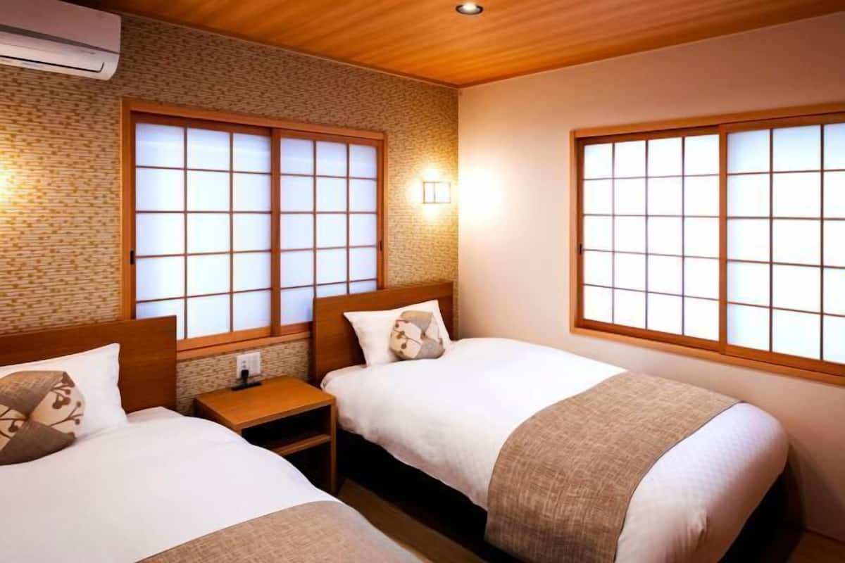 A hotel room with two beds, a wooden headboard, a brick wall, and large windows with wooden frames.