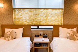 Camera d'albergo con due letti, un comodino, una finestra con persiane e un muro in mattoni.