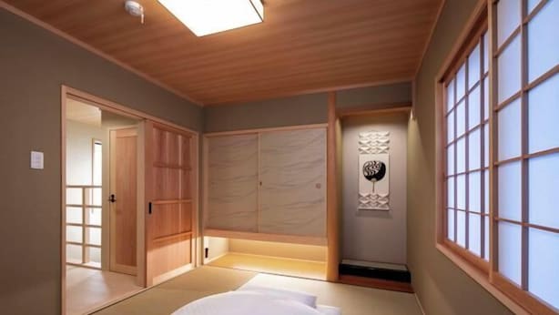 Una stanza tradizionale in stile giapponese con pavimento in tatami, un letto basso in legno, porte scorrevoli e un paravento shoji.