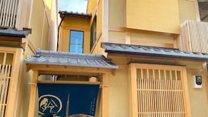 Un edificio tradizionale giapponese con un cancello in legno, un tendone blu con un logo e un tetto in tegole.