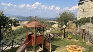 A playground with a slide and climbing structure, surrounded by a stone building and a view of distant hills. - Penthouse 800: elegant and refined apartment located in a historic hamlet (Castiglion Fosco)