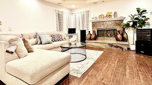 Sala de estar com sofá bege, mesa de centro, lareira e vasos decorativos.