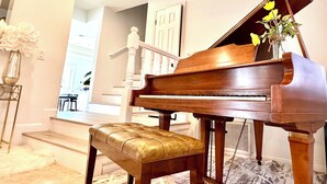Um piano de cauda em um quarto bem iluminado, com piso de mármore, um banquinho e um vaso com flores.