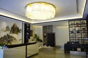 Zona de recepción con candelabro, mostrador de recepción, una pared decorada con un cuadro y una estantería.