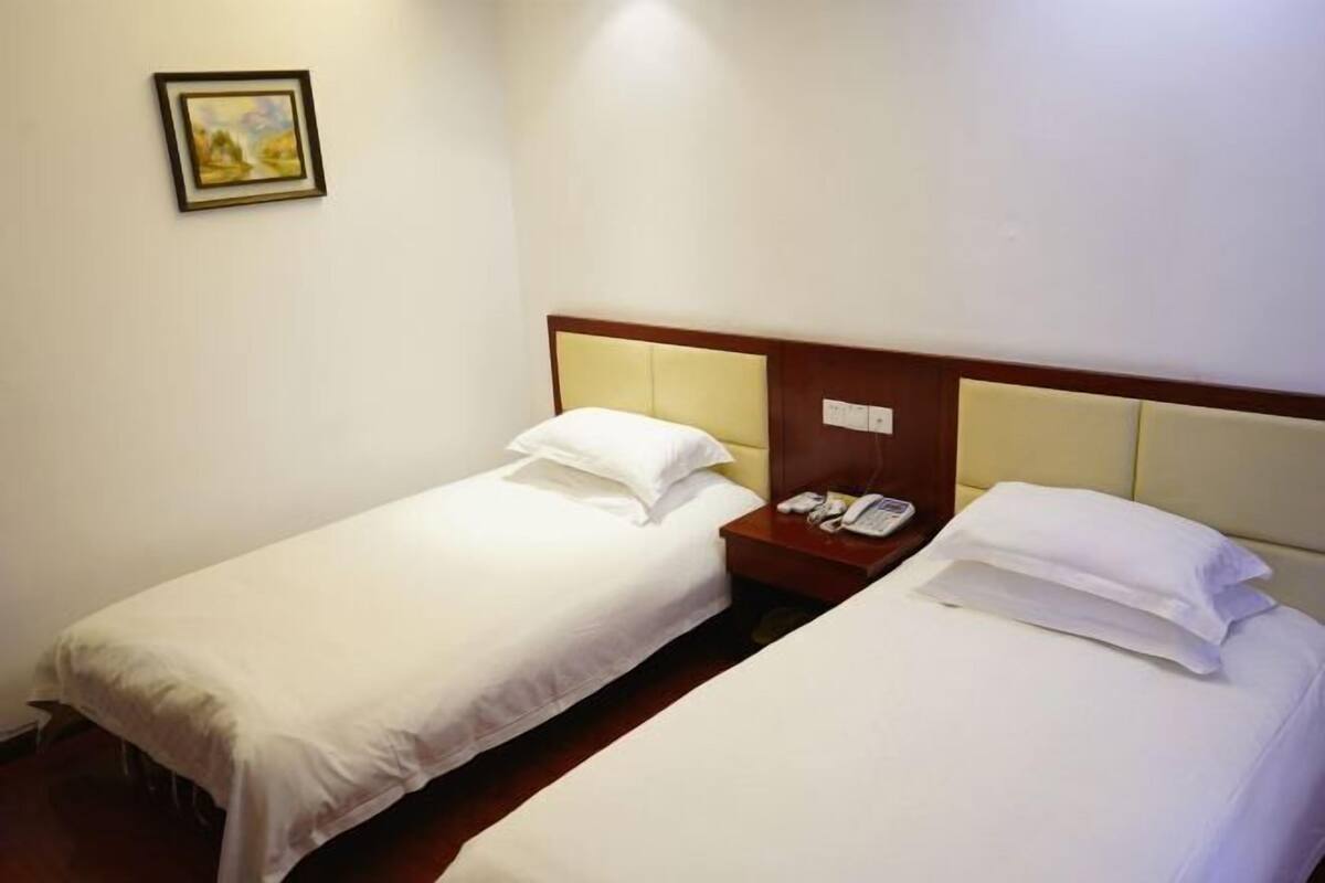 Habitación de hotel con dos camas individuales, una mesita de noche con teléfono y un cuadro en la pared.