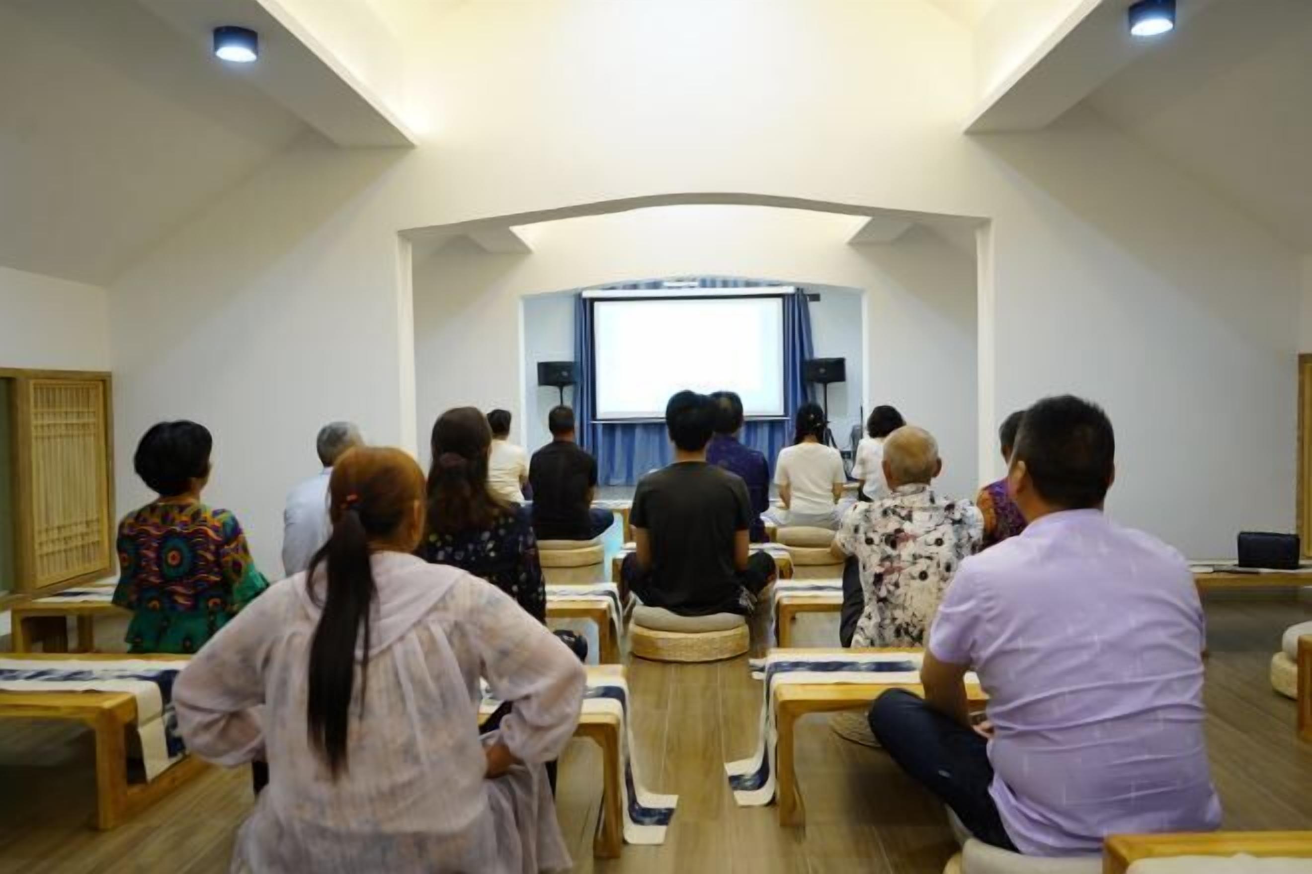 A conference room with rows of chairs facing a stage with a projector screen.