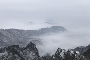 Un paisaje montañoso con picos nevados y un valle cubierto de niebla.
