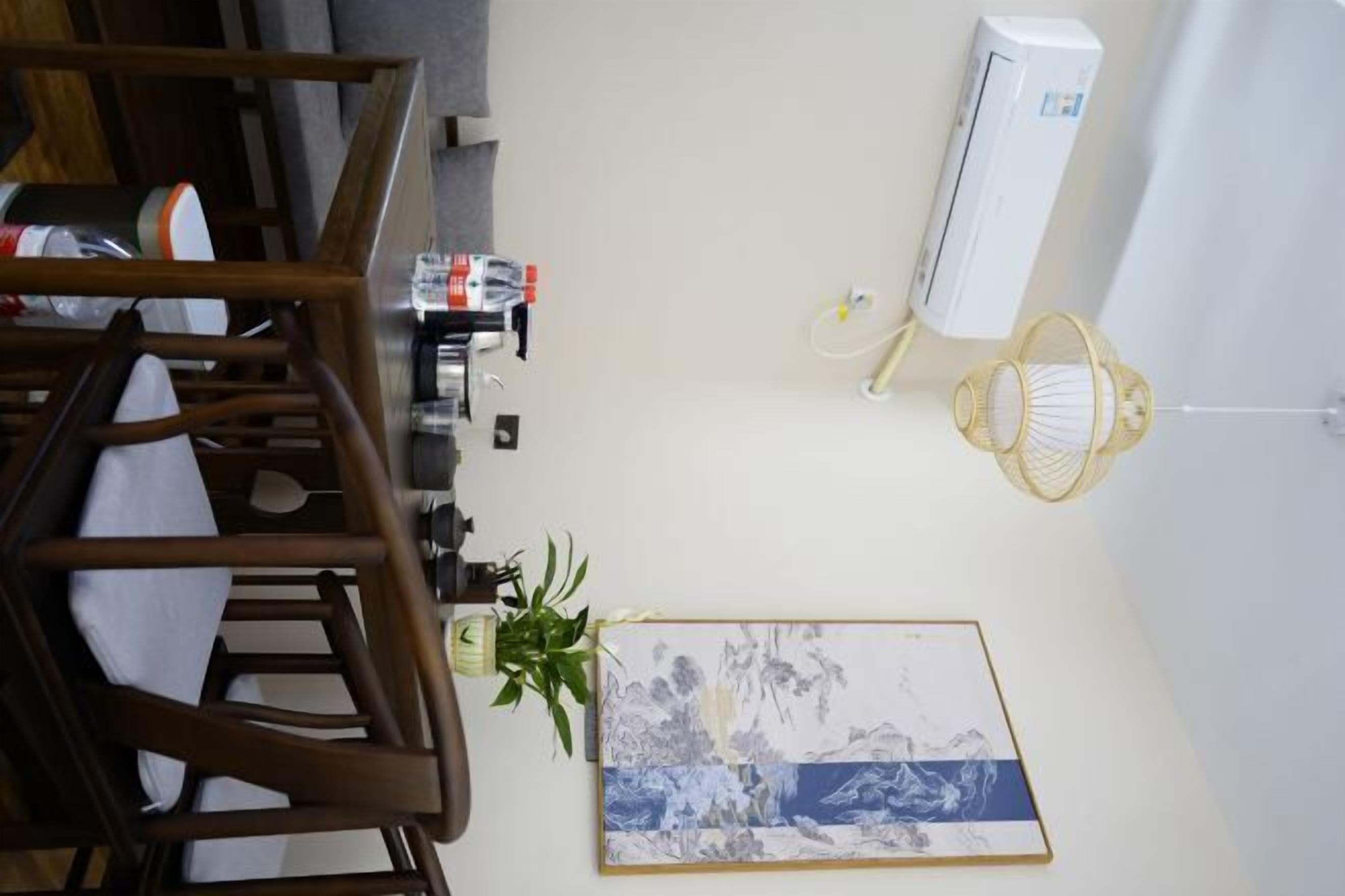 A room with a wooden chair, a wall-mounted air conditioner, a framed artwork, and a hanging light fixture.