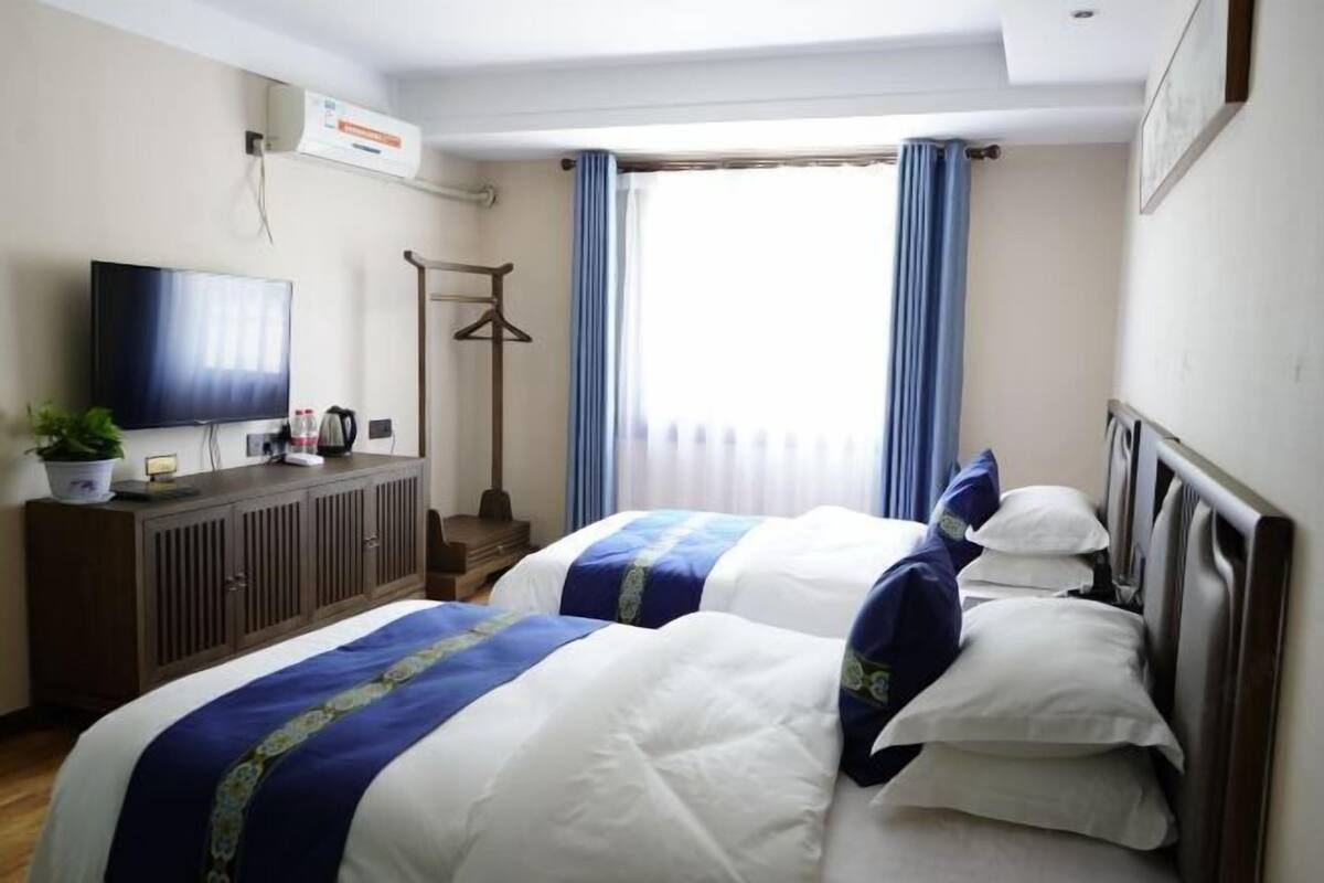 Habitación de hotel con dos camas, televisión, armario y ventana con cortinas.