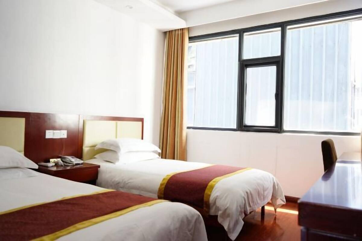 Habitación de hotel con dos camas, un escritorio, una silla, una ventana con cortinas y una mesita de noche con teléfono.