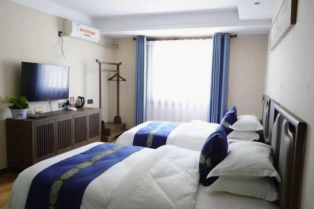 Habitación de hotel con dos camas, televisión, armario y ventana con cortinas.