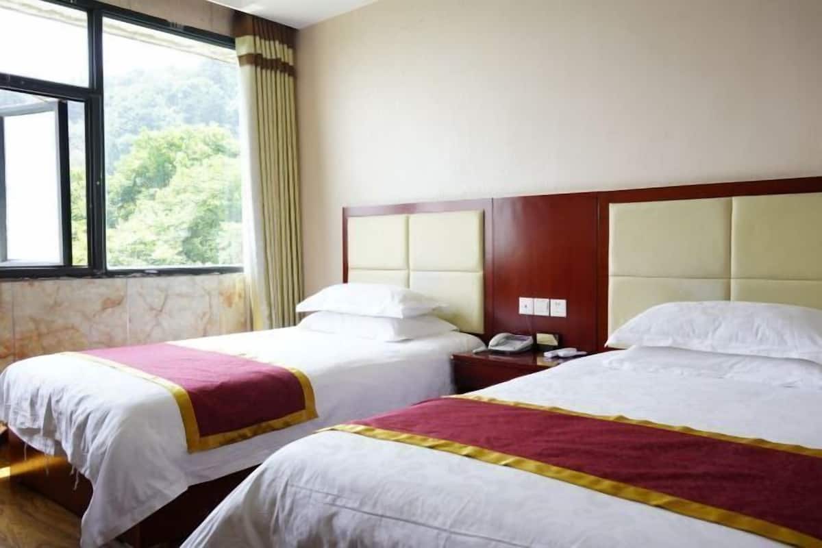 Habitación de hotel con dos camas, cabecero de madera, ventana con cortinas y teléfono en la mesita de noche.