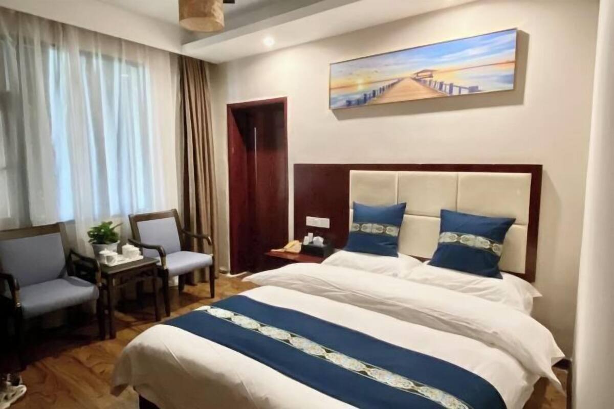 Habitación de hotel con cama, dos sillas, una mesita, una mesita de noche, un cuadro y suelo de madera.