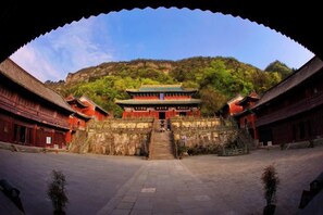 A traditional building with a central staircase leading to a main entrance, surrounded by walls and a hilly landscape. - Taihe Hotel (Danjiangkou)