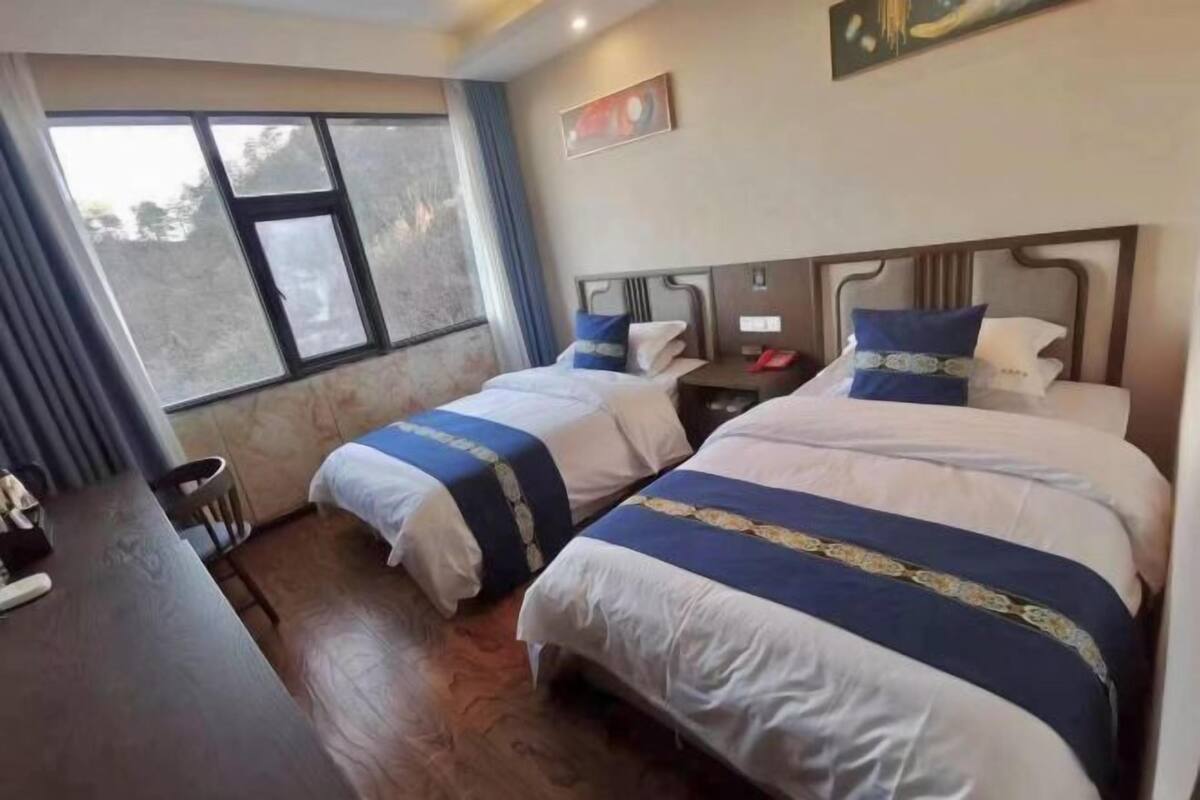 Habitación de hotel con dos camas, un escritorio, una silla y una ventana con vistas.