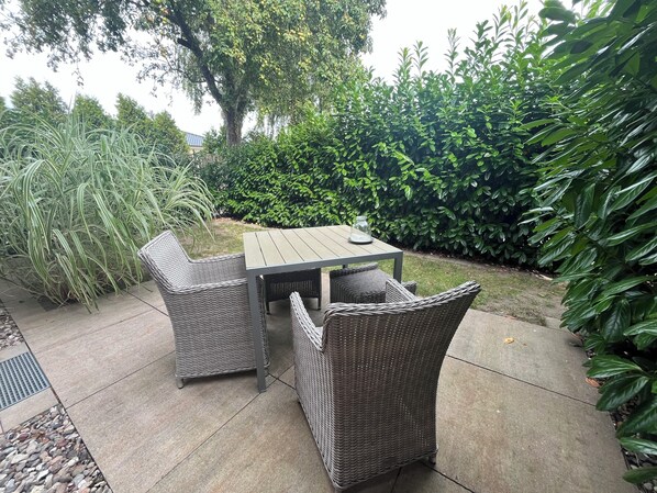 Un patio con tavolo e quattro sedie in vimini, immerso nel verde e con un albero.