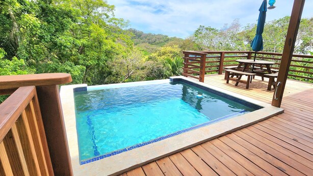 A wooden deck with a swimming pool and a table with chairs. - Stunning Ocean Views, Peaceful, Private Pool, Lush Natural Surroundings (Roatan)