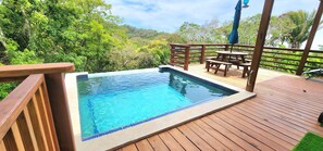 Une terrasse en bois avec une piscine et une table entourée de chaises.
