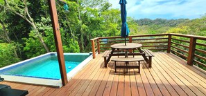 Une terrasse en bois avec une piscine, des tables de pique-nique et une vue sur un paysage boisé.