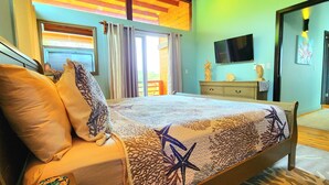 A bedroom with a bed, a dresser, a television, and a window with curtains. - Stunning Ocean Views, Peaceful, Private Pool, Lush Natural Surroundings (Roatan)