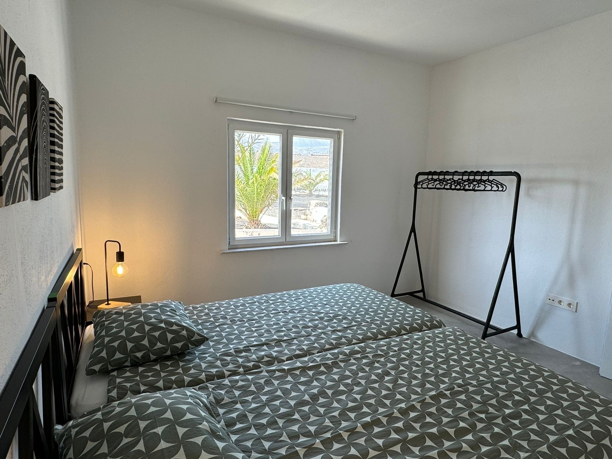 Ein Schlafzimmer mit zwei Betten, einem Fenster, einem Kleiderständer und einer Wandleuchte.