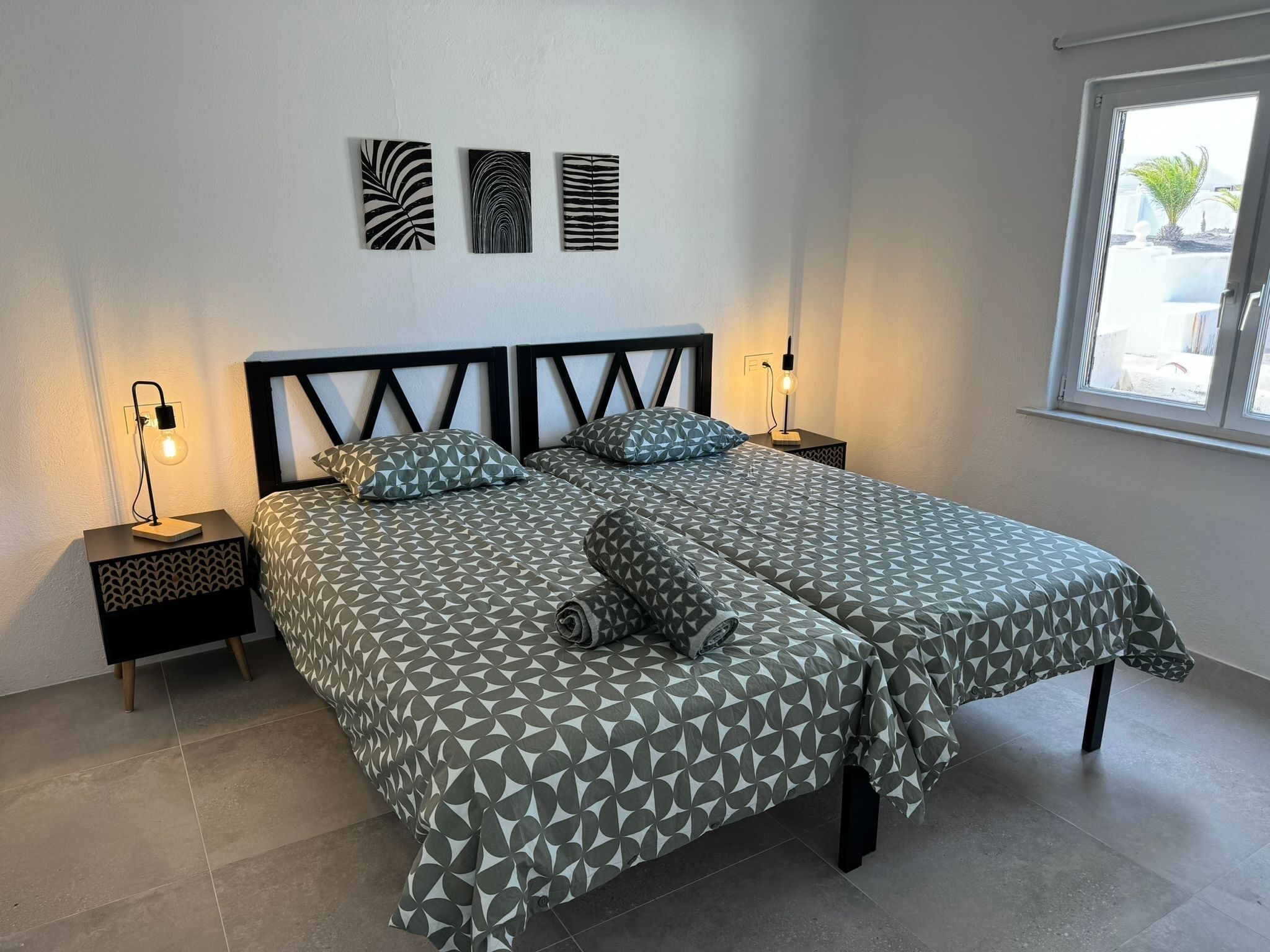 Una cama doble con ropa de cama de diseño geométrico, dos mesitas de noche con lámparas y tres obras de arte en la pared sobre la cama.